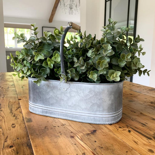 A rustic looking, decorative metal trug/planter with an overly distressed setting and complete with a wooden carry handle.   Perfect for placing in any kitchen with a Country Charm setting.  Please note handles are not fixed.  Size is approximately 30 cm.