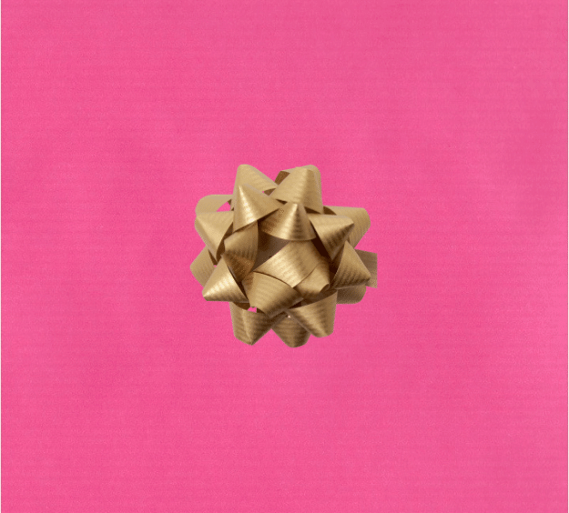 image of a square of pink wrapping paper, the paper is a solid fuchsia kraft paper, in the corner of the gift wrap paper is a gold gift wrapping bow