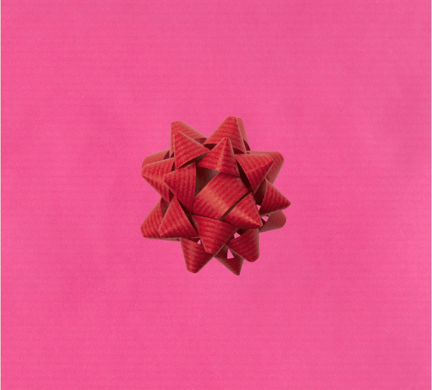 image of a square of pink wrapping paper, the paper is a solid fuchsia kraft paper, in the corner of the gift wrap paper is a green gift wrapping bow