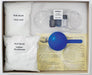 image of the contents of a house of crafts bath bombe craft kit. the box is white on the inside and shows a scoop, some instructions, some moulds, some mini glass jars, citric acid in a plastic bag and sodium bicarbonate in a plastic bag.