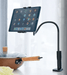 image of a black long neck tablet holder/phone holder. the tablet shows a typical tablet home screen and the phone holder is clamped to a worktop