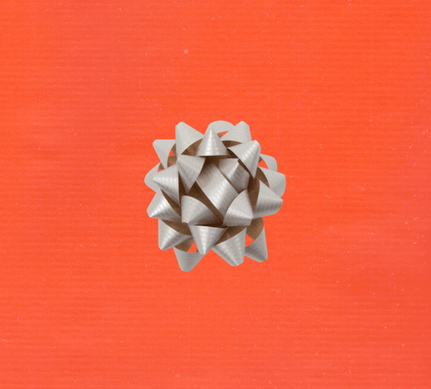 image of a square of wrapping paper, the paper is a solid orange kraft paper, in the centre of the gift wrap paper is a gold paper gift wrapping bow