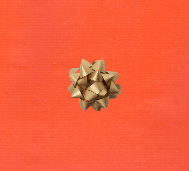 image of a square of wrapping paper, the paper is a solid orange kraft paper, in the centre of the gift wrap paper is a green paper gift wrapping bow