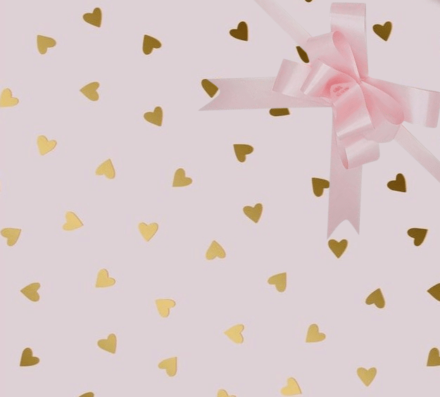 image of a square of wrapping paper, the paper has a pink background and features lots of little gold hearts all over it, in the centre of the gift wrap paper is a gold paper gift wrapping bow