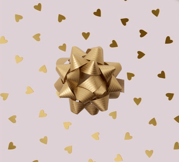 image of a square of wrapping paper, the paper has a pink background and features lots of little gold hearts all over it, in the corner of the gift wrap paper is a silver gift wrapping bow