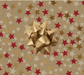 image of a square of wrapping paper, the paper has a gold background and features lots of red, gold and cream stars , in the corner of the gift wrap paper is a silver gift wrapping bow