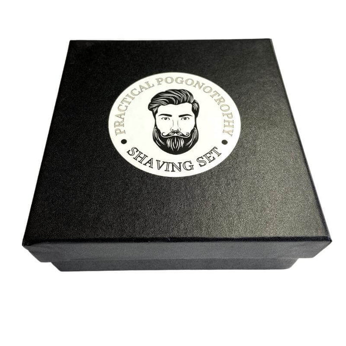 The image is of a practical pogonotrophy shaving razor and brush set. it shows a black gift box with branding circle in the centre containing the words practical pogonotrophy shaving set running round the outside of the circle and an illustrated image of a man with beard and moustache in the centre.