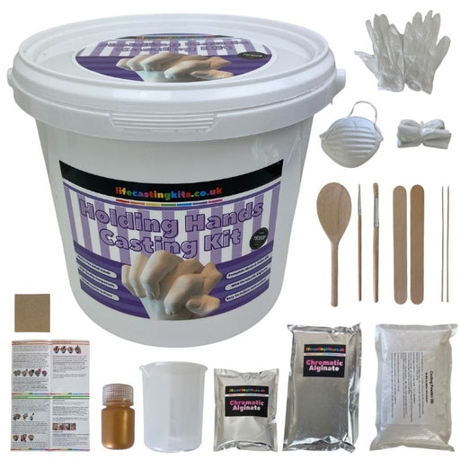 Holding Hands Casting Kit in a white bucket with purple striped label. surrounded by all the contents of the 3d hand casting kit inlcuding chromatic alginate, casting powder, wooden spoon, paint brushes, wooden picks, gloves, mask and aprons, sand paper and full colour instructions.