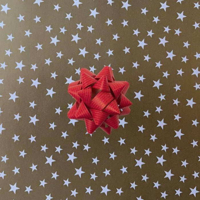 image of a square of wrapping paper, the paper is gold and features lots of solid white stars, in the centre of the gift wrap paper is a silver paper gift wrapping bow