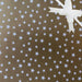 image of a square of wrapping paper, the paper is gold and features lots of solid white stars, in the corner of the gift wrap paper is a light pink gift wrapping bow