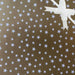 image of a square of wrapping paper, the paper is gold and features lots of solid white stars, in the corner of the gift wrap paper is a light pink gift wrapping bow