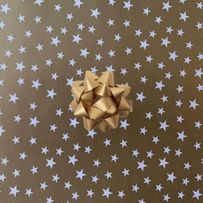 image of a square of wrapping paper, the paper is gold and features lots of solid white stars, in the corner of the gift wrap paper is a bright blue gift wrapping bow