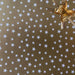 image of a square of wrapping paper, the paper is gold and features lots of solid white stars, in the corner of the gift wrap paper is a light blue gift wrapping bow