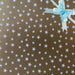 image of a square of wrapping paper, the paper is gold and features lots of solid white stars, in the corner of the gift wrap paper is a green gift wrapping bow