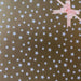 image of a square of wrapping paper, the paper is gold and features lots of solid white stars, in the corner of the gift wrap paper is a gold gift wrapping bow